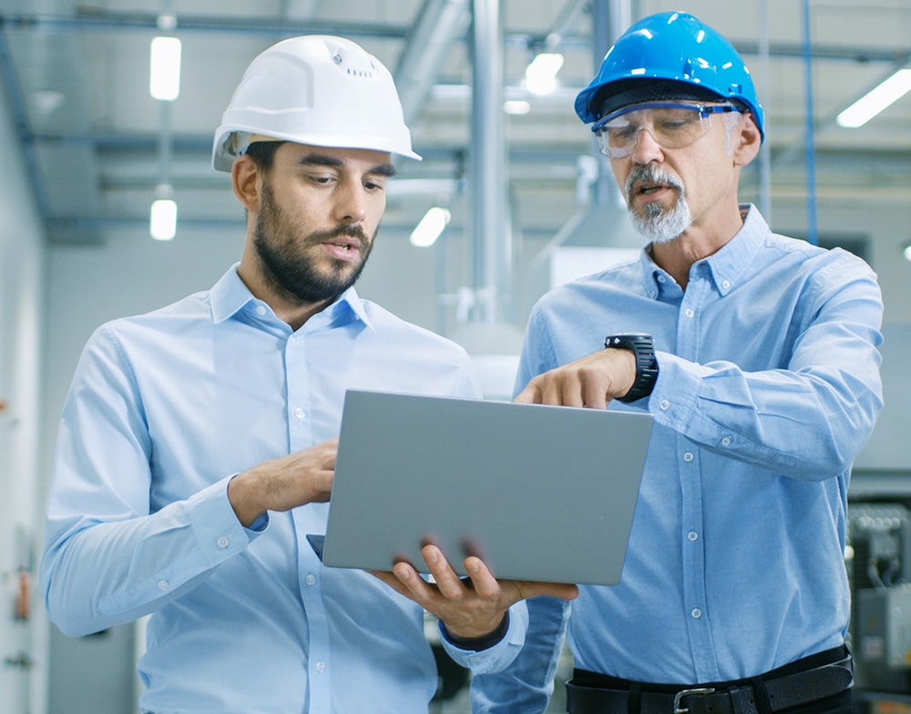 Two manufacturing business professionals review work on a laptop while walking factory floor